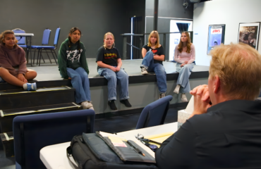 Students performing Frozen Jr. on stage with Arendelle castle backdrop and sparkling snow effects